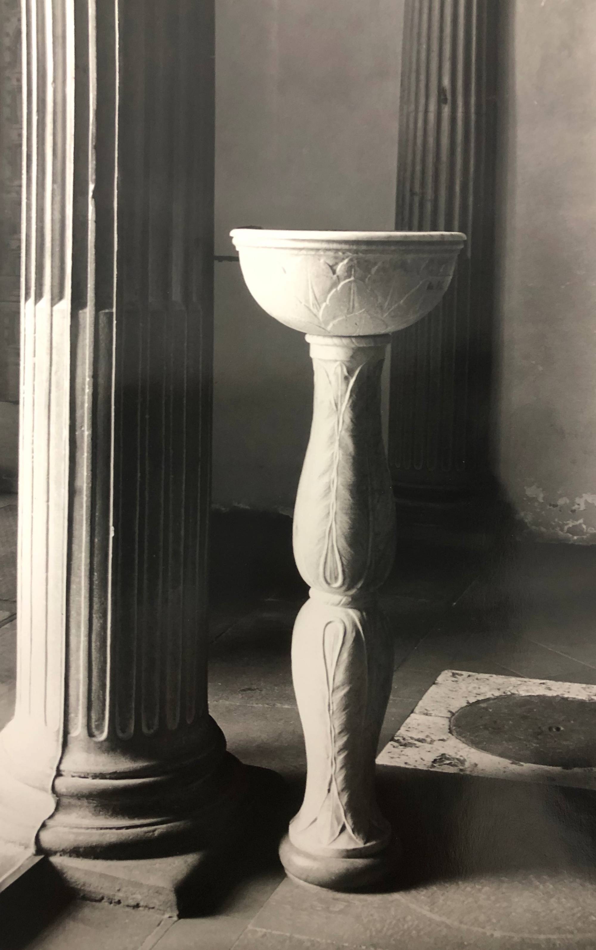 black and white photograph of font of holy water next to column